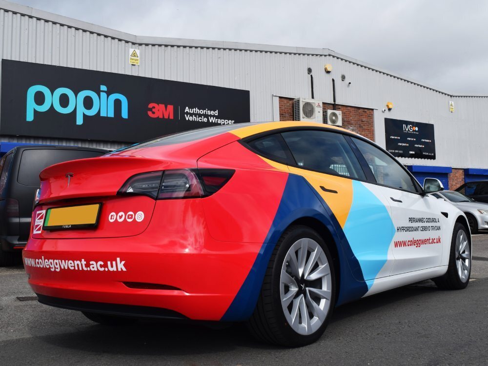 Tesla Model 3 electric company car with rear Coleg Gwent branded partial wrap outside Popin in Cardiff.