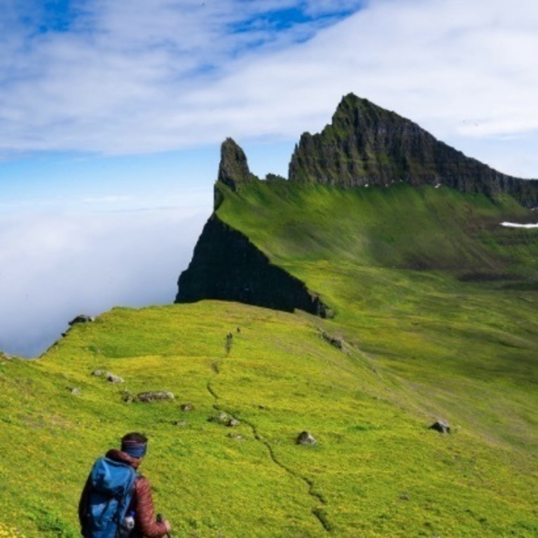 Hikers walking along grassy ridge toward Hornbjarg in Hornstrandir Nature Reserve, Westfjords Iceland