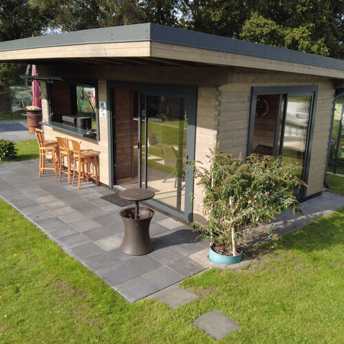 Stylish timber pavilion with a modern flat roof and an open-plan design, featuring a mix of natural wood and glass for a contemporary aesthetic. The pavilion includes large sliding glass doors that open onto a sleek stone-tiled patio, providing seamless indoor-outdoor flow. A built-in bar area with wooden bar stools offers a perfect space for entertaining, while potted plants and a manicured lawn with stepping stones enhance the natural surroundings. Designed and installed by Forever Timber, this pavilion combines elegance, functionality, and expert craftsmanship, making it an ideal addition to any outdoor living space.