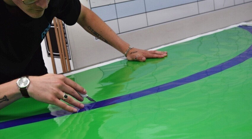 Vehicle wrap technician cutting vinyl material before installation onto a Renault lorry.