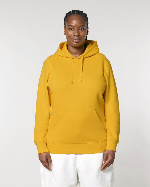 Woman in bright yellow organic hoodie and white trousers, showcasing ethical streetwear on a plain neutral background.
