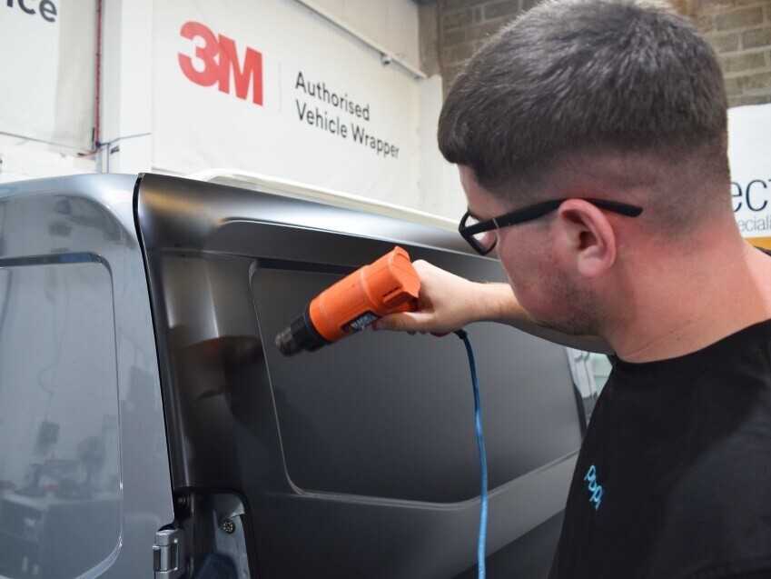 Technician carefully installing a vehicle vinyl wrap onto a van.