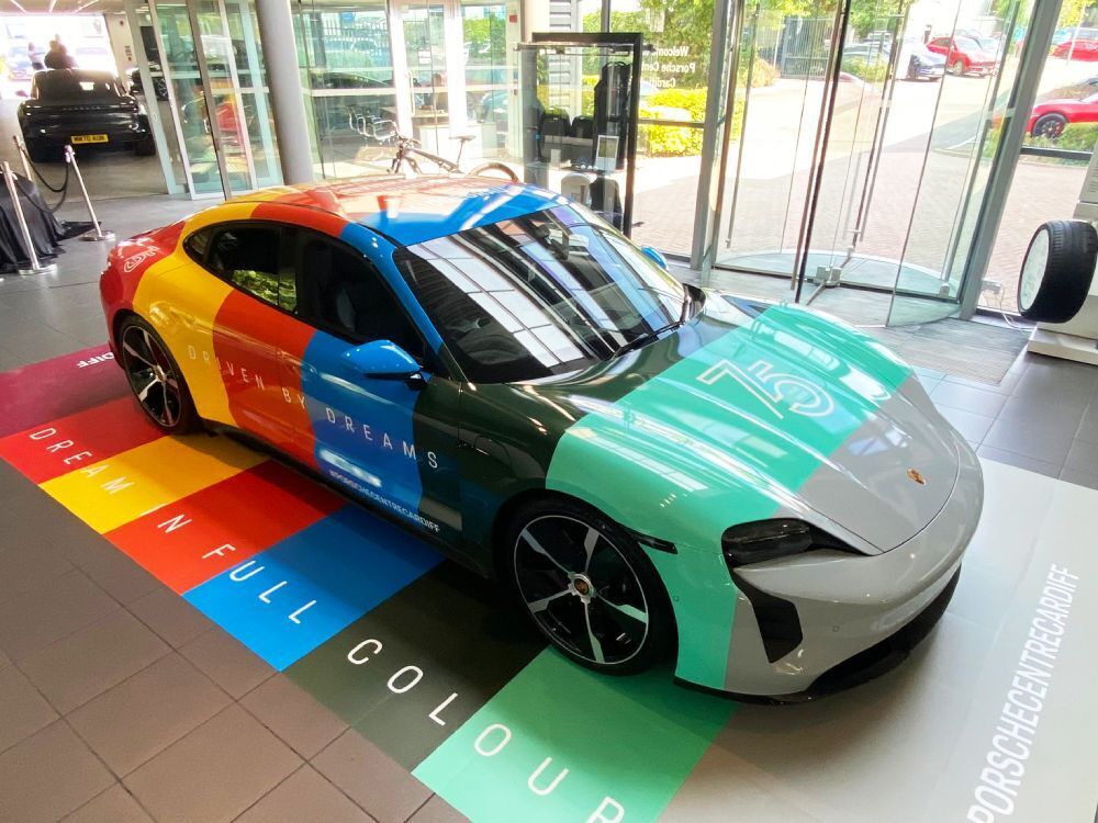 Aerial view of company Porsche Taycan with colourful full livery.