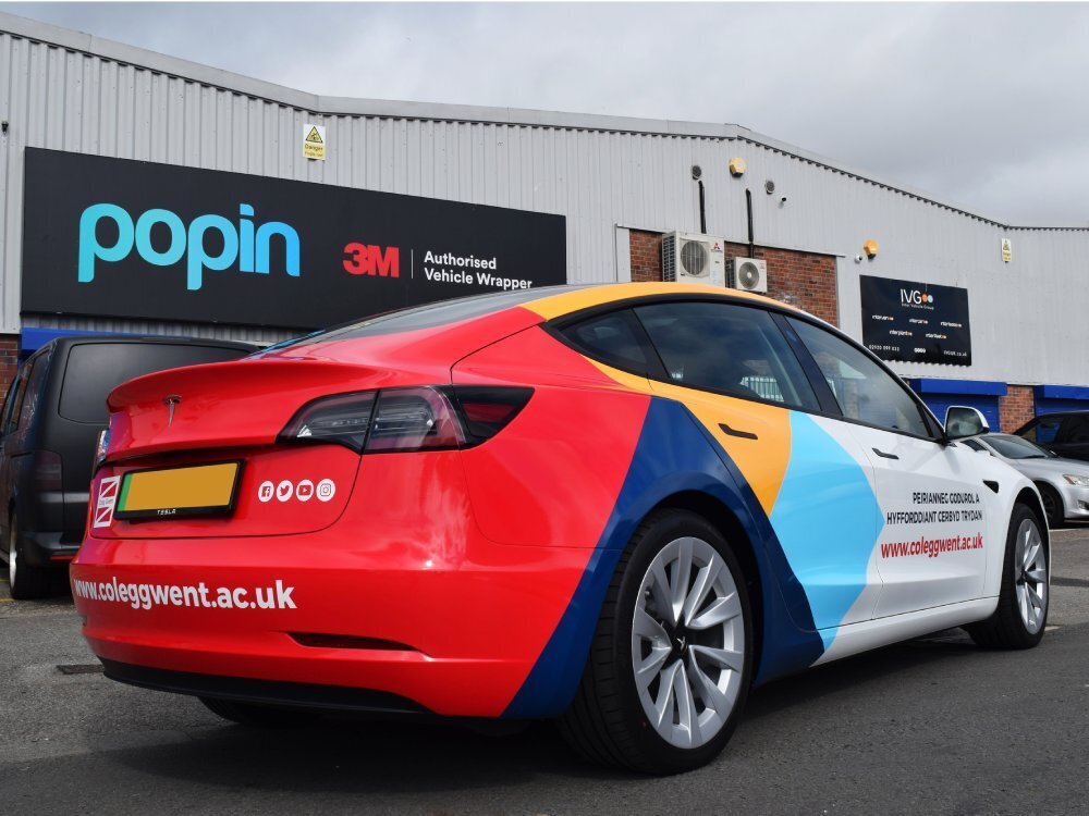 Rear view of Tesla Model 3 company car with colourful partial wrap and branded vinyl graphics outside Popin in Cardiff.