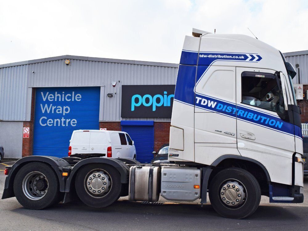 Side profile of a white Volvo lorry with new blue branded vehicle vinyl graphics outside Popin in Cardiff.