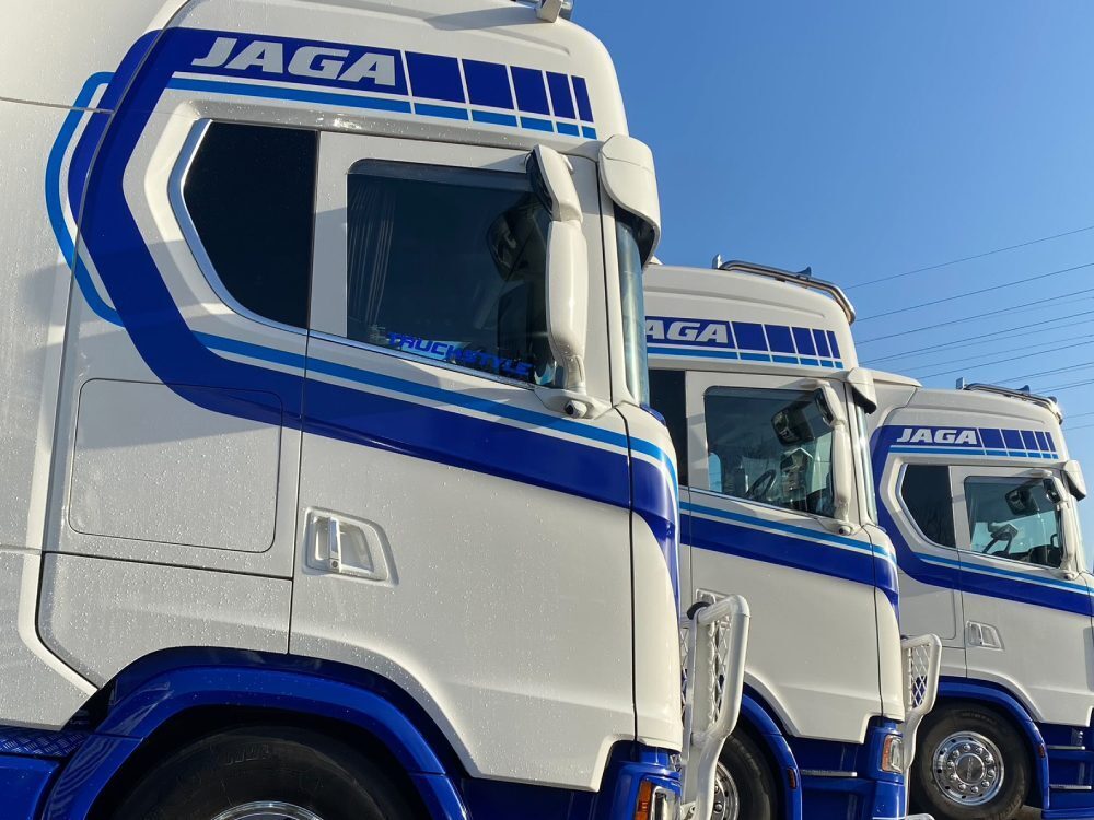Matching blue vehicle vinyl graphics on a fleet of white Scania trucks.