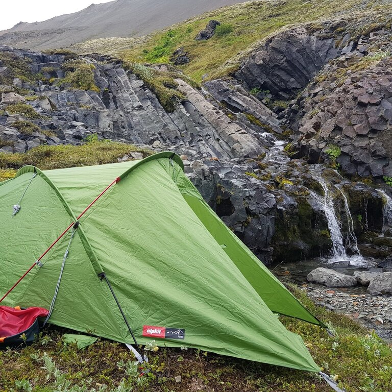 Green tent pitched beside a small stream in the Hornstrandir backcountry, Iceland