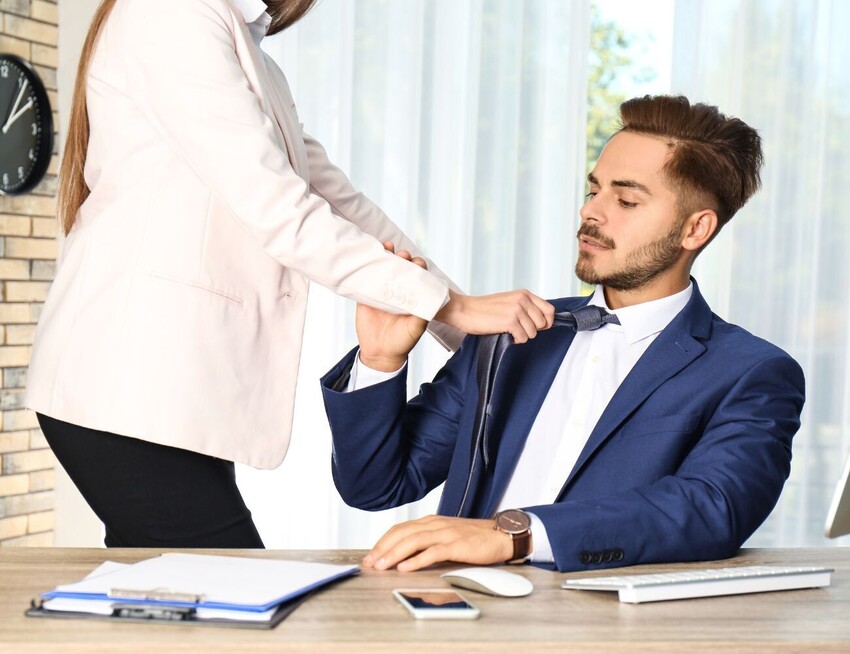 New sexual harassment laws 2026 - a female manager pulling a male colleague's tie towards her as she stands over him