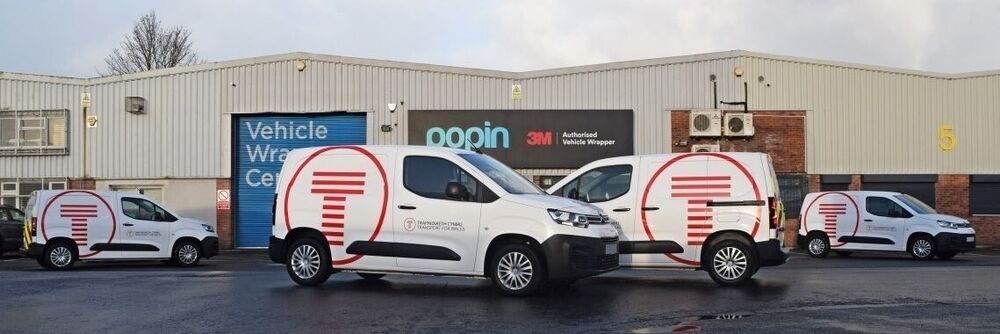 Fleet of company vans with consistent branded vinyl graphics parked outside Popin vehicle wrap facilities in Cardiff.