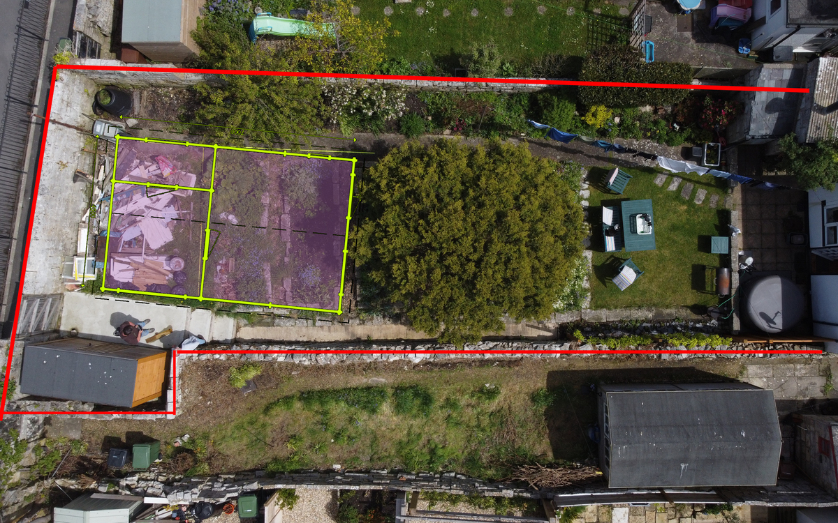 "Overhead aerial view of a residential property featuring a garden area divided into distinct zones. The red outline marks the boundaries of the property, while a section highlighted in yellow and purple indicates a specific area, potentially designated for construction or renovation. The property includes a central pathway, green lawn with patio furniture, and surrounding greenery. The image also shows various structures, including sheds and outbuildings. This visual is likely used for planning or project management purposes."
