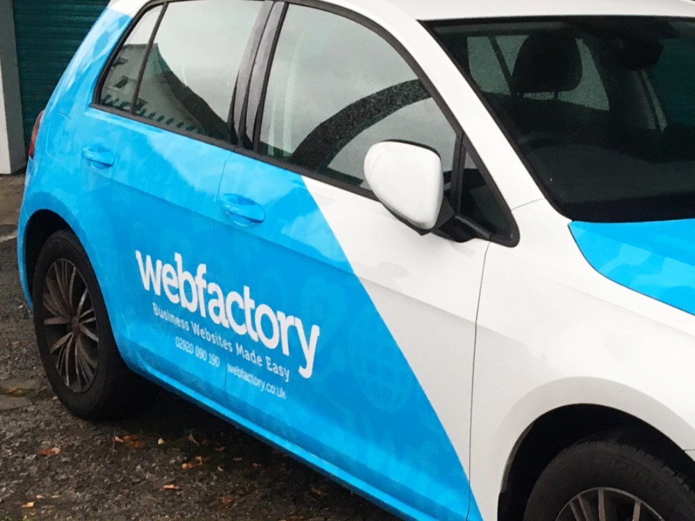 Branded vehicle wrap on rear side door of Volkswagen Golf company car.