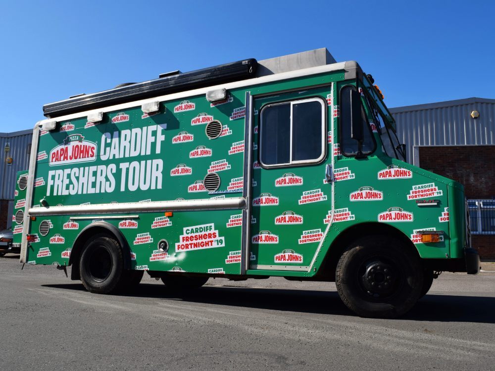 Side profile of a GMC truck with a green Papa Johns pizza vehicle wrap and graphics.