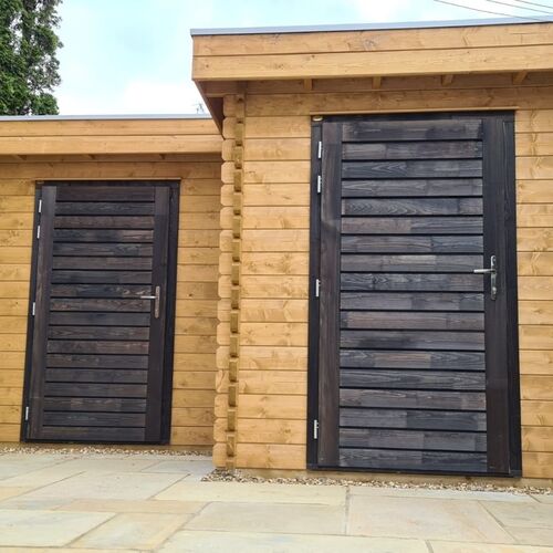 Modern timber garage crafted from high-quality wood with a flat roof and sleek design. Features include two sturdy, dark-stained timber doors with horizontal paneling and steel handles, providing a contemporary contrast against the natural wood walls. The structure is set on a durable paved base, enhancing functionality and style. This premium garage was supplied by Lugarde and thoughtfully designed and installed by Forever Timber, combining elegance, practicality, and expert craftsmanship.