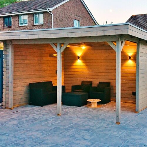 A bespoke garden gazebo supplied by Lugarde and designed and installed by Forevertimber. This stylish structure features a natural timber finish with a flat roof and open-fronted design, supported by sturdy wooden posts with decorative bracing. The back and side walls are enclosed with horizontal wooden panels, creating a cozy and private space. Warm wall-mounted lights add ambiance, making it a perfect area for evening relaxation or entertaining. The gazebo is set on a large stone-paved base, providing durability and a clean, polished look. Furnished with comfortable black seating, it combines practicality and elegance to enhance any outdoor space.