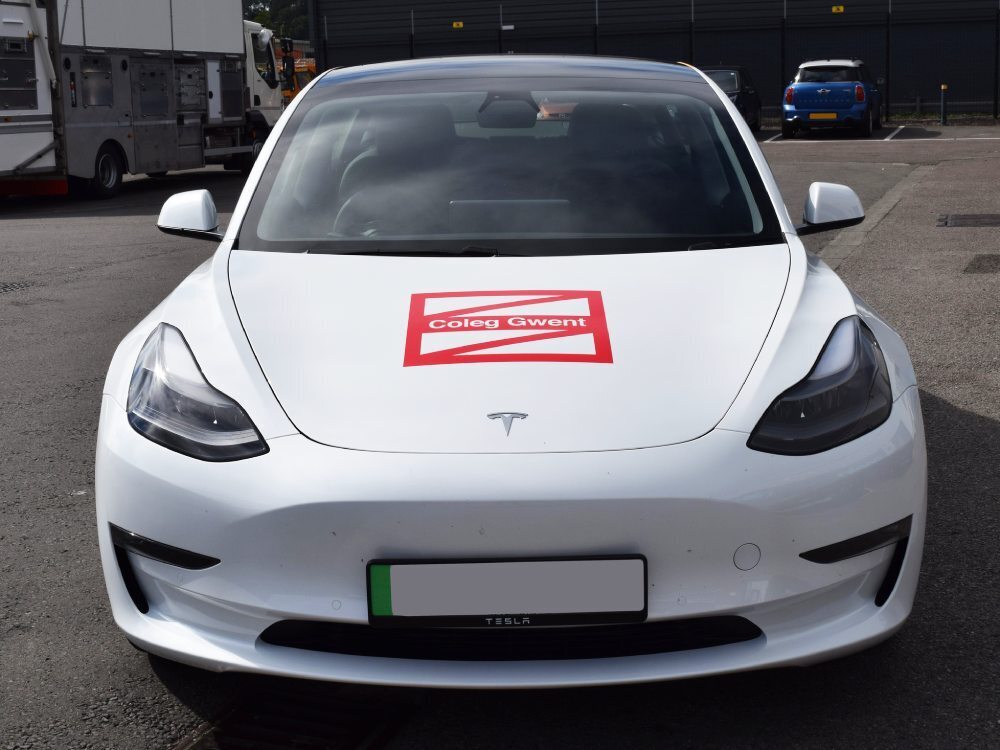 Red Coleg Gwent logo vinyl graphics on front bonnet of white Tesla Model 3 electric company car.