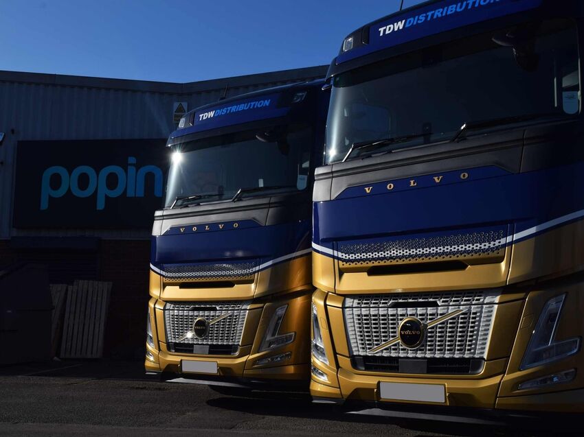 Fleet of Volvo trucks with matching blue and gold vinyl wraps outside Popin.