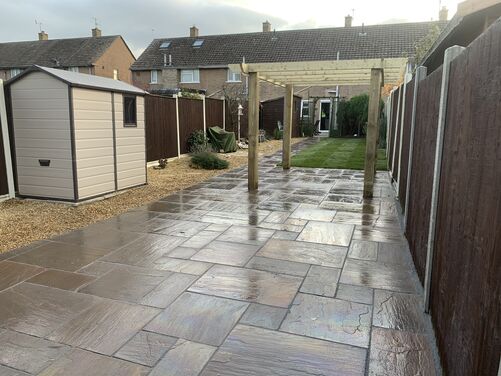 This is a clean and well-maintained backyard featuring a paved patio area, gravel borders, a small garden shed, and a pergola.