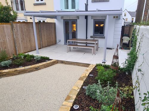 Beautifully designed backyard featuring a modern patio with a covered seating area, surrounded by landscaped garden beds with stone edging. The space includes a mix of gravel and greenery, creating a low-maintenance yet stylish outdoor living area perfect for dining and relaxation