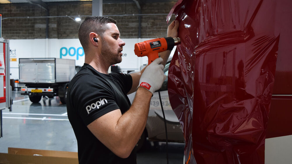 3M Select Graphic Specialist applying a red vehicle wrap to a van at Popin Graphics