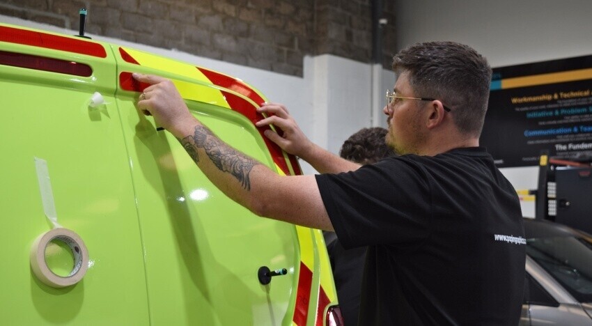 Vehicle wrap technician installing chevron vinyl graphics onto rear of a Peugeot Partner van at Popin in Cardiff.