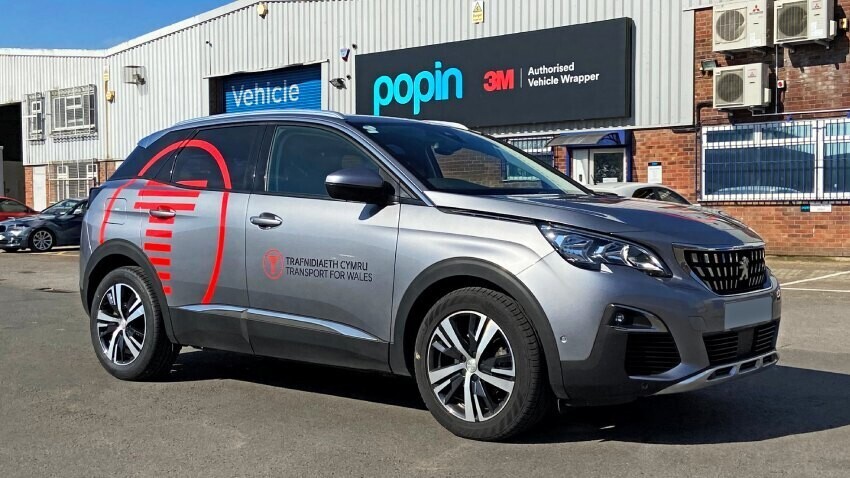 Red branded vinyl graphics on silver company Peugeot 3008 outside Popin in Cardiff.