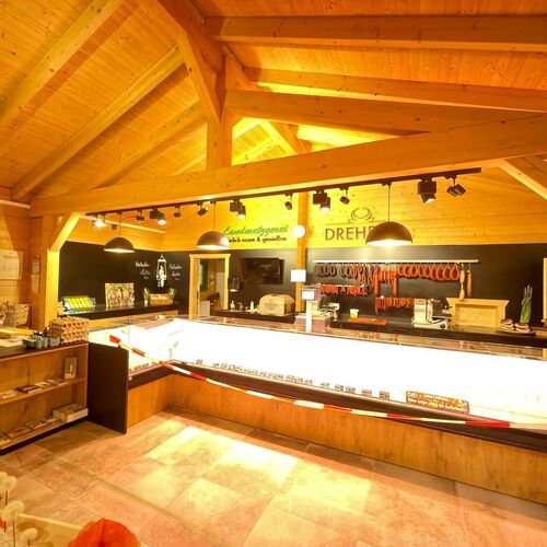 Warm and inviting interior of a timber commercial building, featuring exposed wooden beams and ceilings that showcase expert craftsmanship. The space is designed as a retail shop or deli, with a brightly illuminated glass display counter for showcasing products. Black chalkboard-style walls with handwritten signage add a rustic and personalized touch, while shelves and hooks offer additional display and storage options. The ambient lighting highlights the natural wood tones, creating a cozy and welcoming atmosphere. Designed and installed by Forever Timber, this space blends functionality with charm, making it perfect for customer-facing businesses