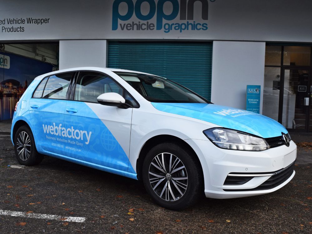 Partial blue branded vehicle wrap and graphics on white Volkswagen Golf company car outside Popin in Cardiff.