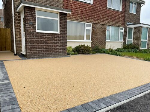 Modern driveway featuring a sleek resin-bound surface framed with dark brick edging for a polished and durable finish. The design complements the brick exterior of the house, offering a low-maintenance and visually appealing solution that enhances the property's curb appeal