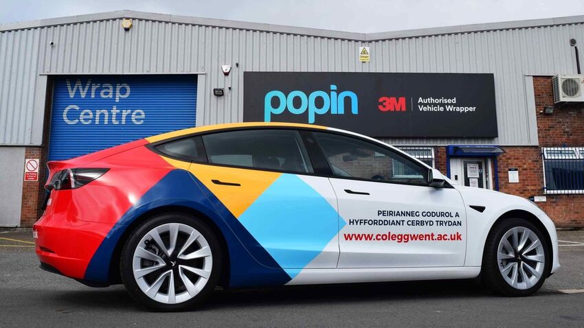 White company car with colourful partial wrap at the rear end of the vehicle and vinyl graphics towards the front end.