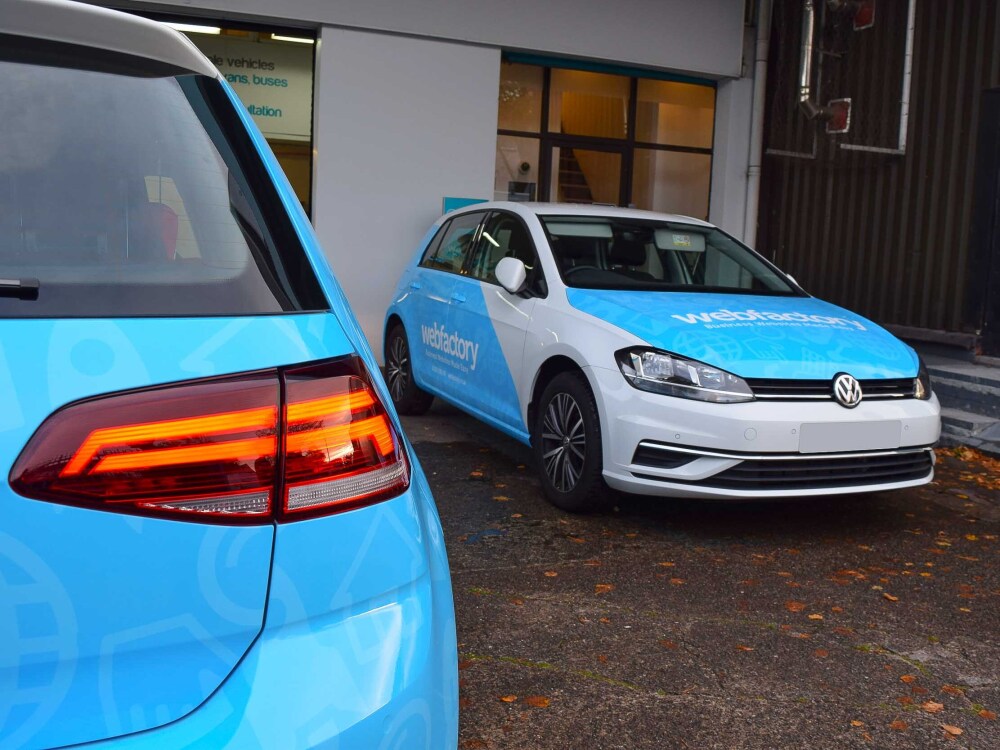 Fleet of Volkswagen Golf company cars with matching branded blue and white vehicle wraps and graphics.