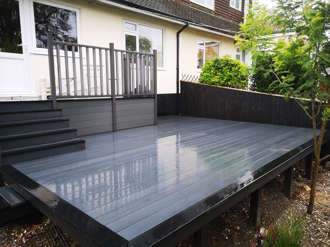 Modern elevated decking area featuring sleek grey composite boards with matching railings and black trim for a contemporary look. The deck is complemented by clean landscaping and provides a stylish extension of the home, ideal for outdoor living and entertaining.