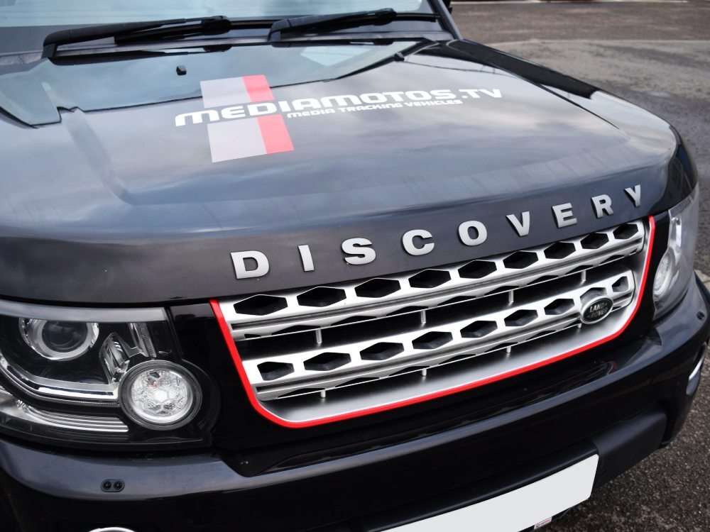 Branded vinyl graphics and red grille trim applied to front of black company Land Rover Discovery.