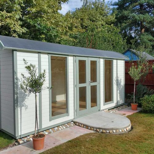 Elegant timber garden building featuring a curved roof, painted in a soft white finish with sage green accents on the doors and windows. The structure includes tall glass panels and double doors, allowing ample natural light to illuminate the interior. A circular stone step with decorative pebble edging leads to the entrance, adding a touch of charm. Surrounded by a neatly landscaped garden with potted olive trees and a lush lawn, this garden building is both functional and aesthetically pleasing. Designed and installed by Forever Timber, it offers a versatile space ideal for use as a home office, studio, or relaxation area.