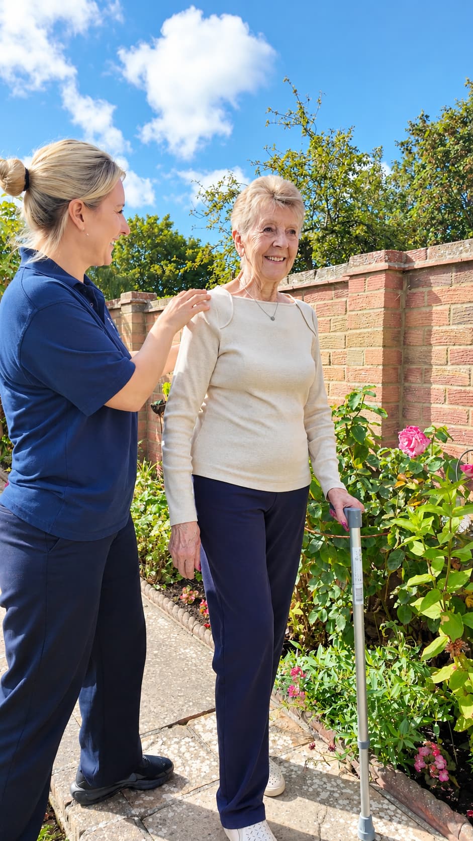 Physiotherapist supporting an older adult practising walking with a stick in her garden