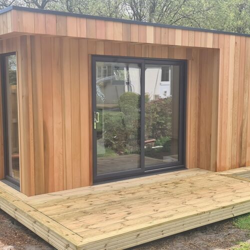 Contemporary timber-framed building designed for comfort and functionality, featuring full insulation and fully fitted interiors, including a shower and toilet. The exterior is elegantly clad in premium red cedar, adding a warm and natural aesthetic to the structure. With large sliding glass doors and a wooden deck, this building seamlessly integrates indoor and outdoor spaces, making it an ideal choice for a modern garden office, studio, or guest suite.