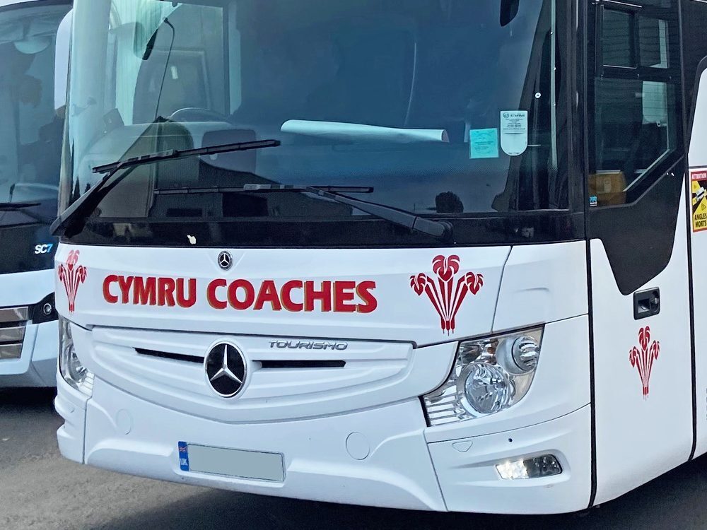 White livery and red Cymru Coaches branded vehicle graphics on front of Mercedes Tourismo coach.