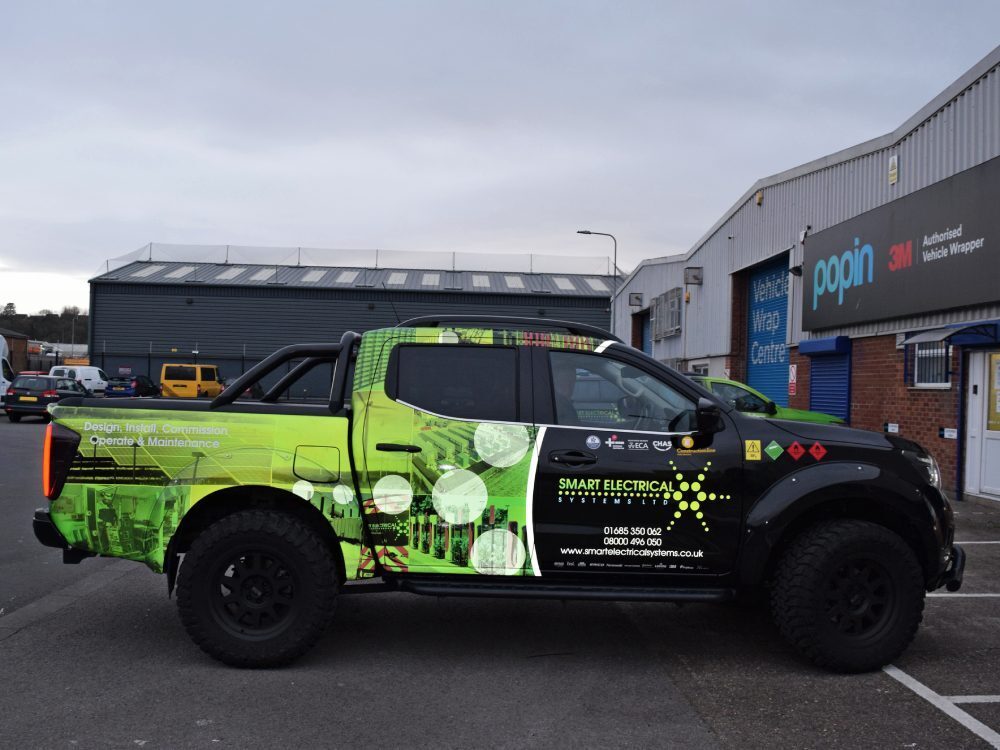 Black company Nissan Navara with green reflective livery and graphics outside Popin wrap centre in Cardiff.