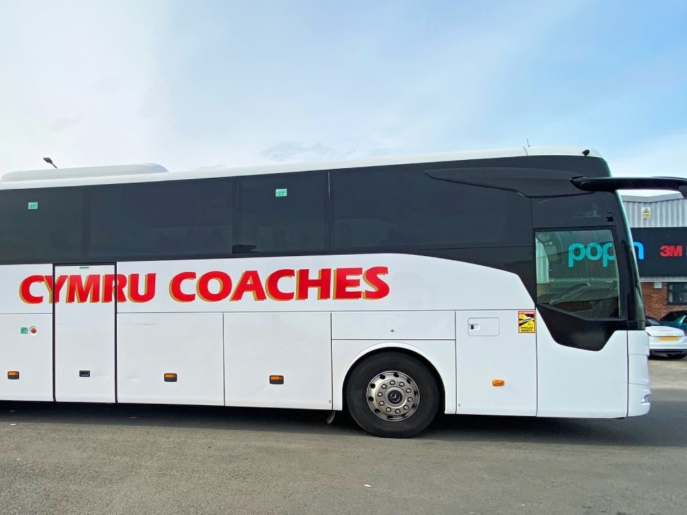 Side of Mercedes Tourismo with white wrap and red Cymru Coaches branded graphics.