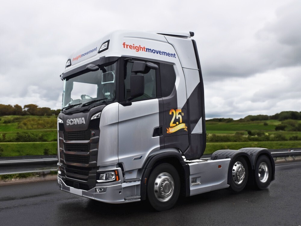 Scania lorry cab with silver vehicle wrap and vehicle graphics driving on a road.