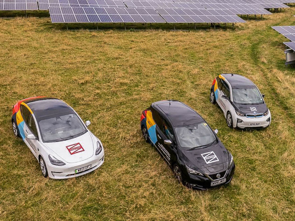 Fleet of company electric cars with branded vehicle graphics parked on grass.