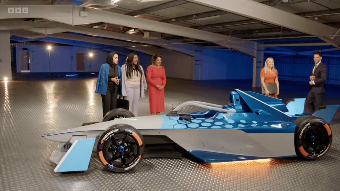 A group of women standing next to a race car on the apprentice
